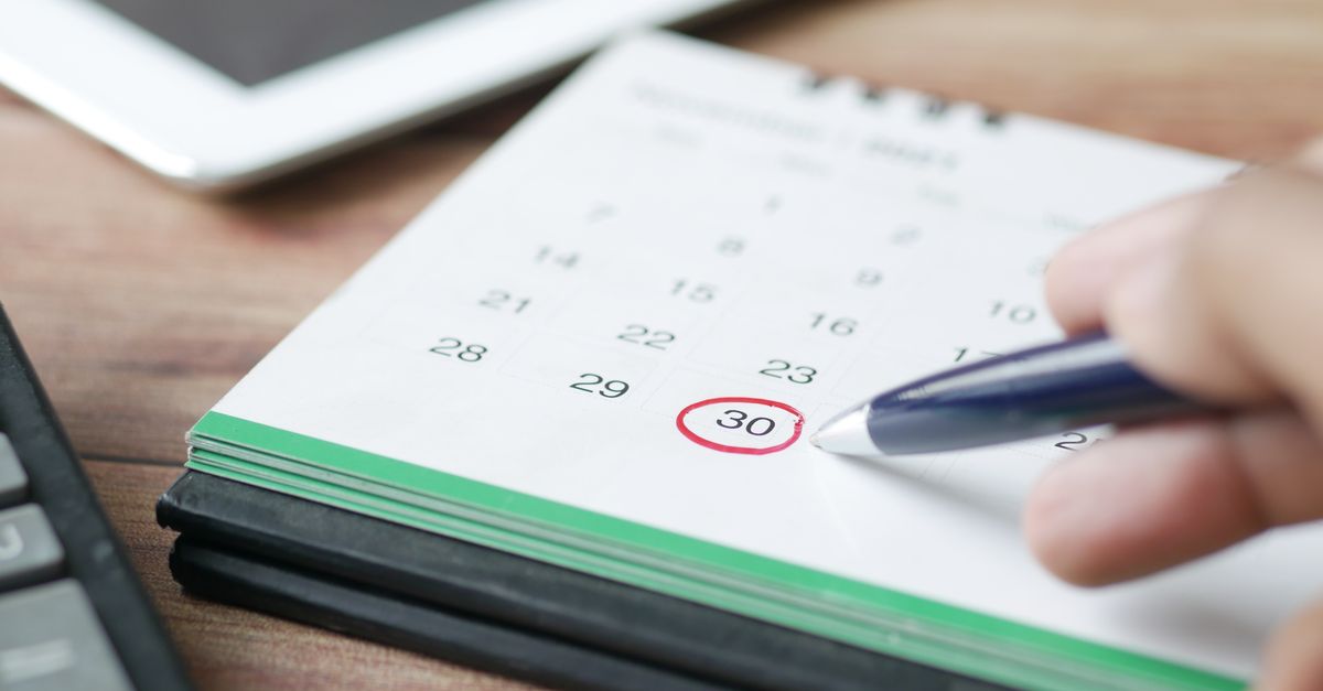 Close-up shot of a hand marking a date on a calendar with a pen, emphasizing planning and scheduling.
