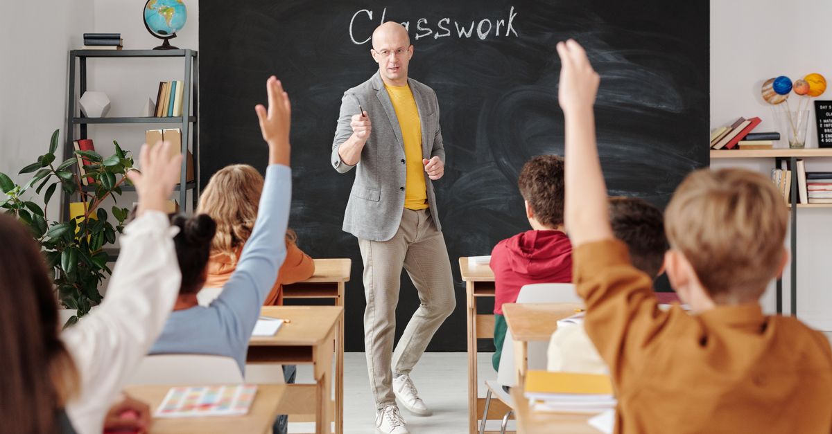 Teacher interacting with students raising hands in a classroom setting.