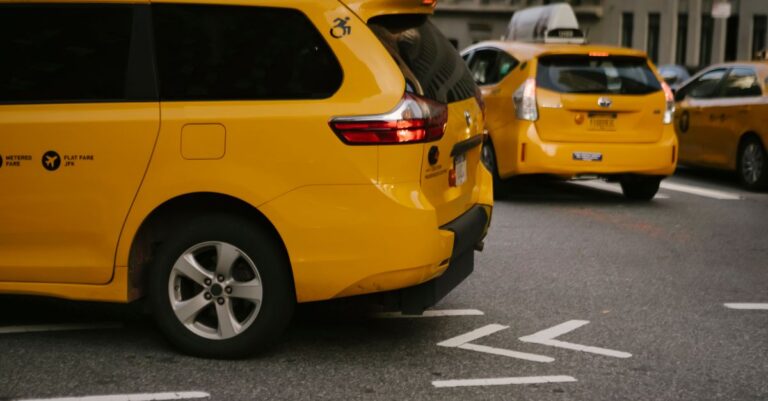 Modern yellow crossover taxi cars riding on asphalt road near commercial buildings in city