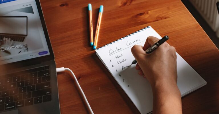 Photo of a person writing a list of online courses on a notepad next to a laptop.
