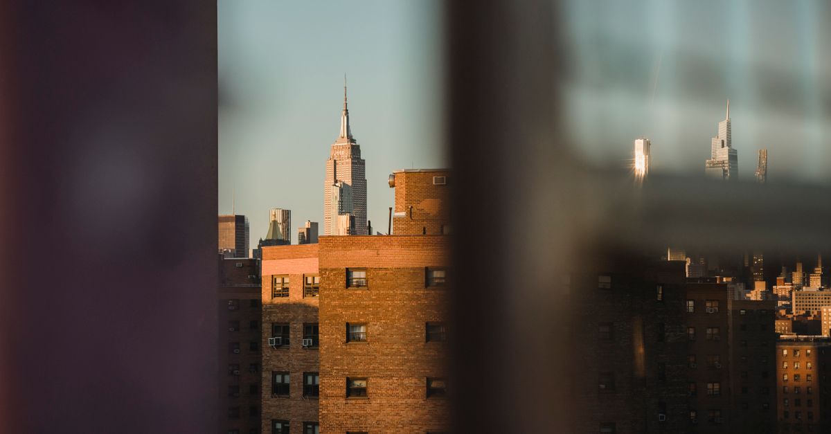 Through fence view of aged multistory house exteriors under light sky in town in evening