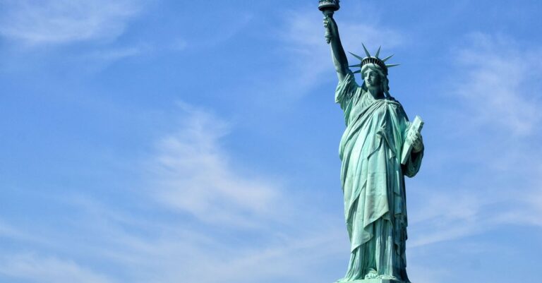 The Statue of Liberty stands tall on Liberty Island under a clear blue sky, symbolizing freedom.